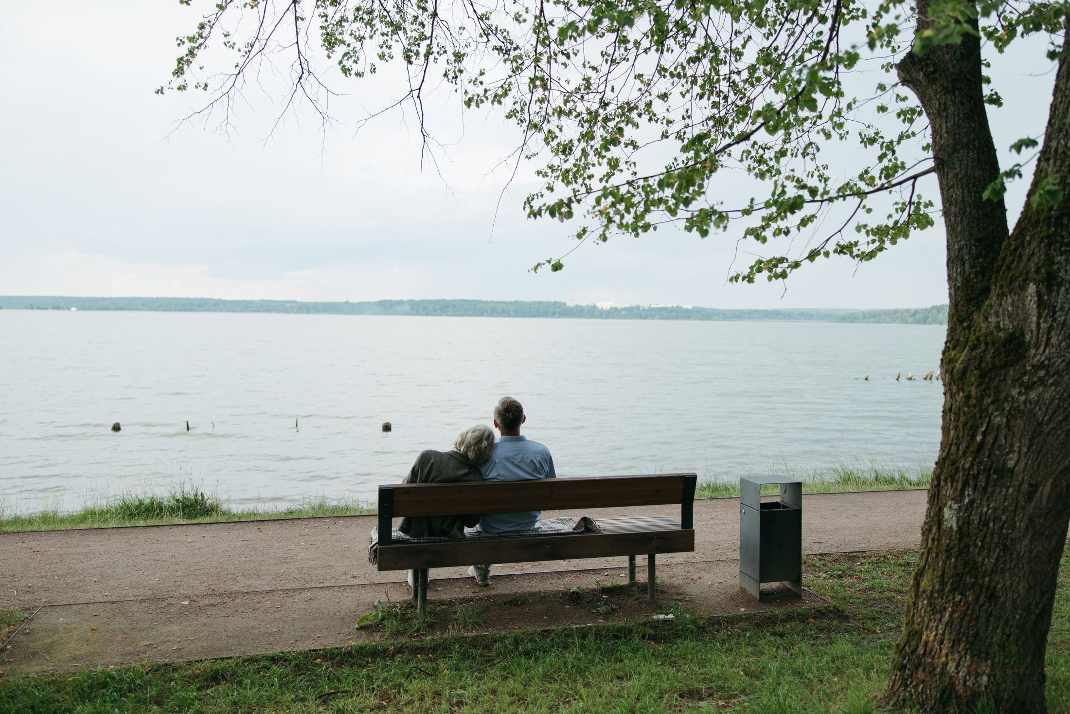 An older couple sitting together on a bench, looking out over open water
