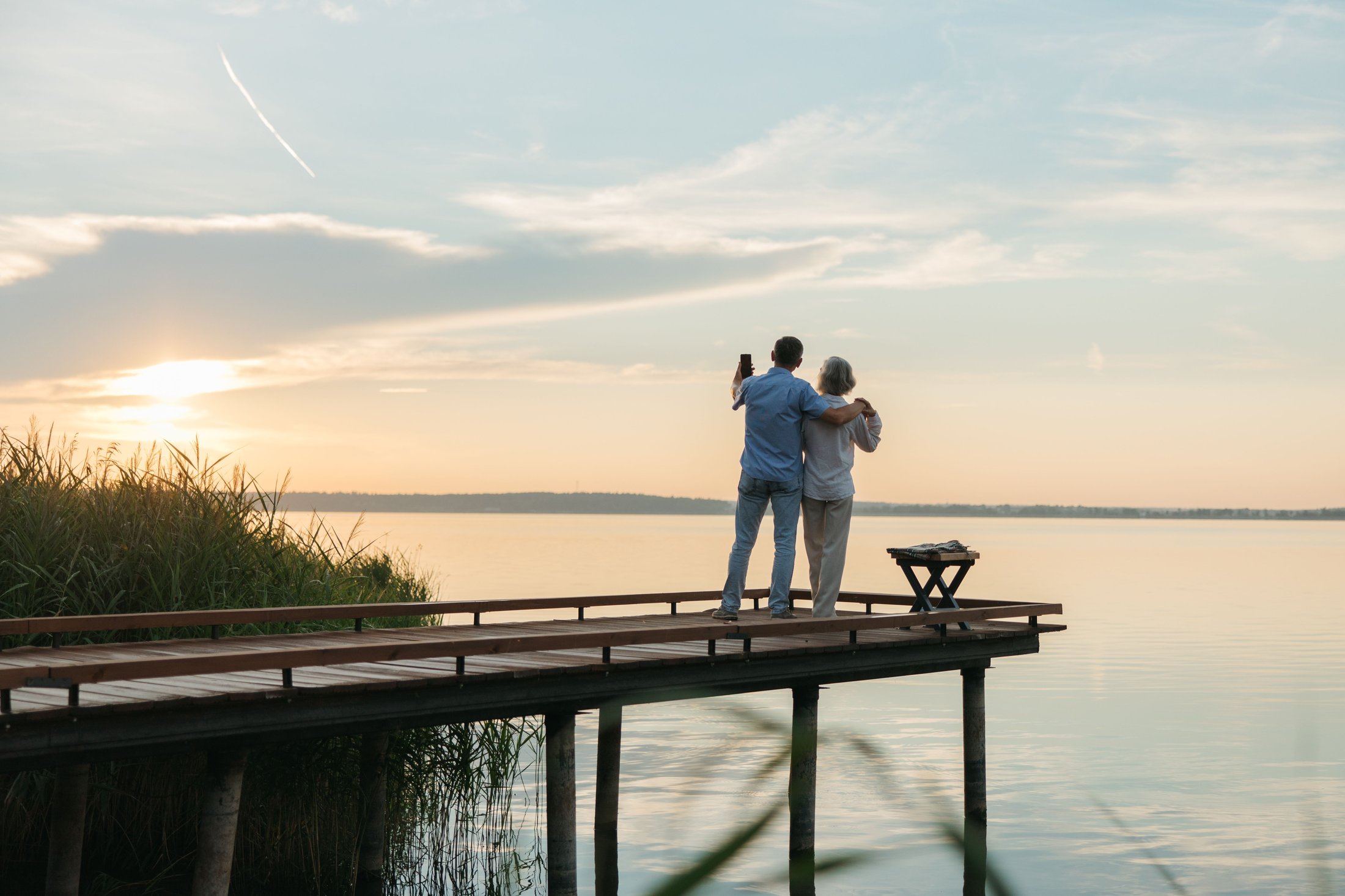 An older couple standing together at the end of a dock at sunset