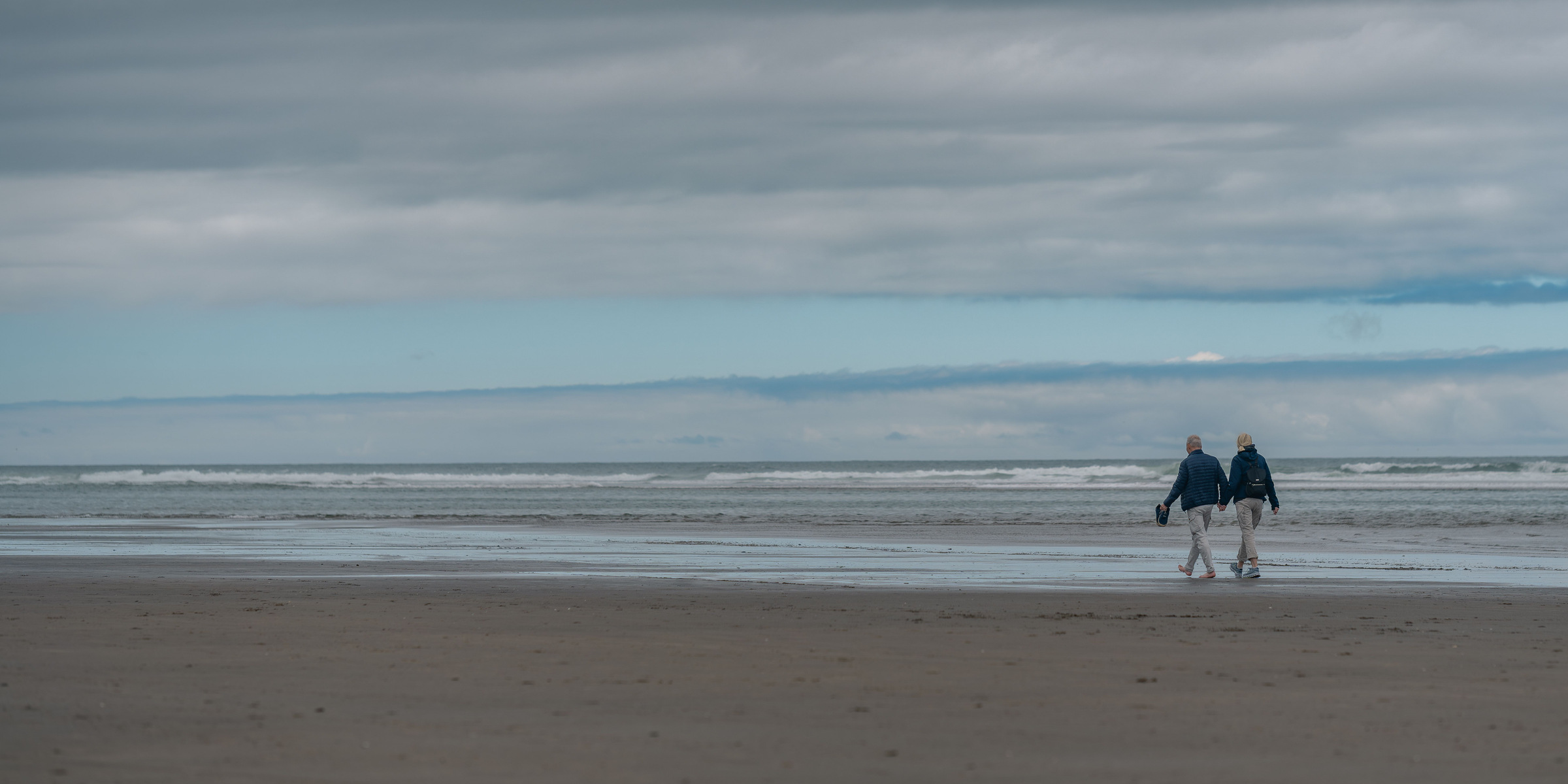 A retired couple walking together on a wide, empty beach